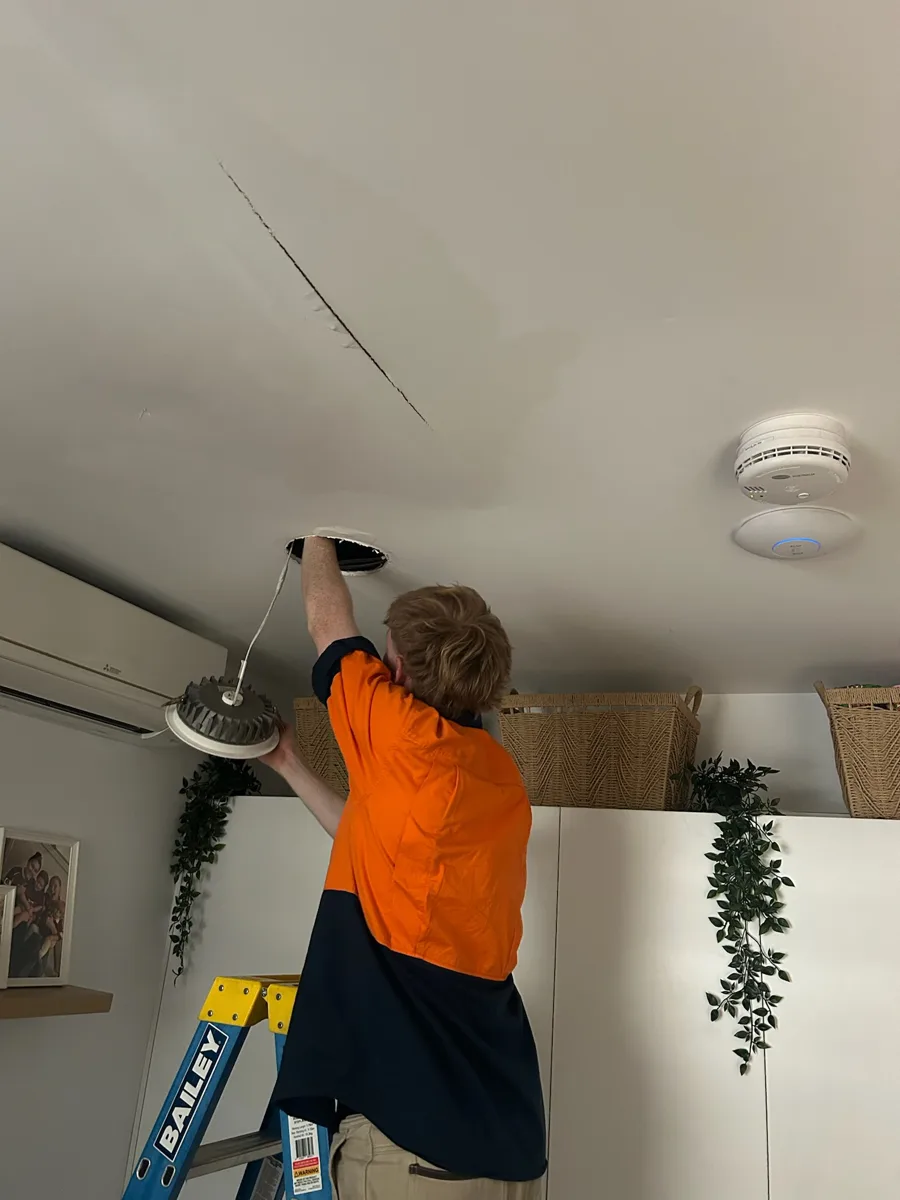 A KTM electrician in a Brisbane home with photoelectric smoke alarms fitted to the ceiling